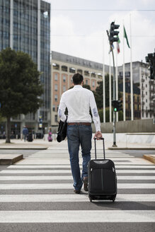 Rückenansicht eines Geschäftsmannes mit Koffer beim Überqueren der Straße - MAUF00880
