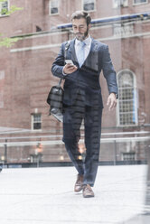 USA, New York City, businessman walking in Manhattan looking at cell phone - UUF08934