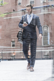 USA, New York City, Geschäftsmann geht in Manhattan spazieren und schaut auf sein Handy - UUF08934