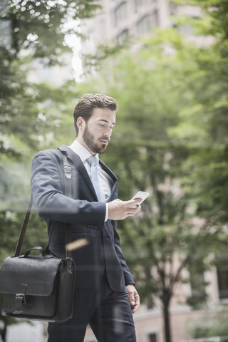 Geschäftsmann geht und schaut auf sein Handy, lizenzfreies Stockfoto