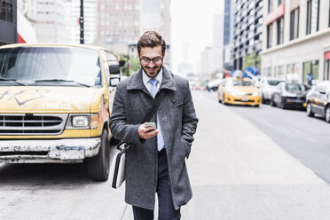 USA, New York City, smiling businessman with cell phone on the go - UUF08969
