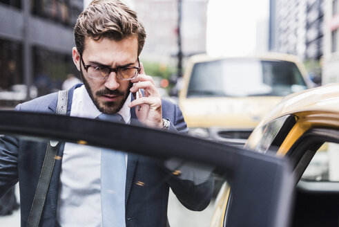 USA, New York City, Geschäftsmann in Manhattan telefoniert beim Einsteigen in ein Taxi - UUF08971