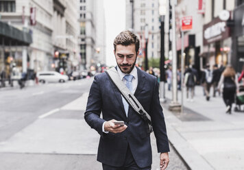 USA, New York City, businessman walking in Manhattan looking at cell phone - UUF08991