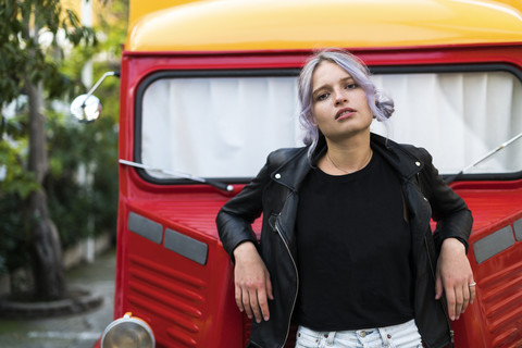 Porträt einer jungen Frau mit gefärbtem Haar, die sich an einen Lieferwagen lehnt, lizenzfreies Stockfoto