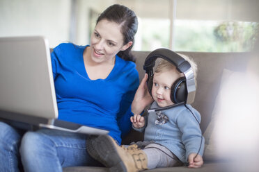 Mutter mit einem kleinen Mädchen, das Kopfhörer trägt und einen Laptop zu Hause benutzt - ZEF11504