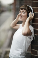 Lächelnde junge Frau hört Musik mit weißen Kopfhörern - TAMF00765