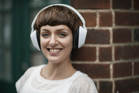 Porträt einer lächelnden jungen Frau, die mit weißen Kopfhörern Musik hört, lizenzfreies Stockfoto