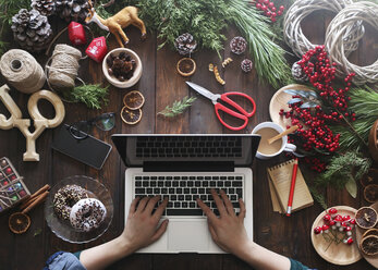 Woman working with laptop at her desk covered with utensils for creating Advent wreaths, partial view - RTBF00480