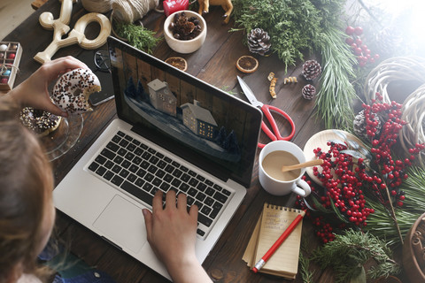 Frau isst Bagel und arbeitet mit Laptop, Teilansicht, lizenzfreies Stockfoto