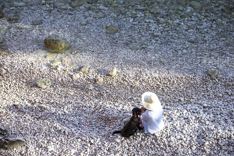 Draufsicht auf eine Frau, die mit ihrem Hund am Strand sitzt, lizenzfreies Stockfoto