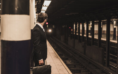 Junger Geschäftsmann wartet am Bahnsteig einer U-Bahn-Station - UUF08997