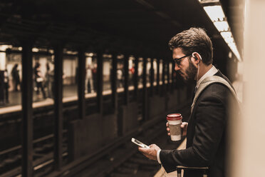Junger Geschäftsmann, der am Bahnsteig einer U-Bahn-Station wartet und ein Smartphone benutzt - UUF09004