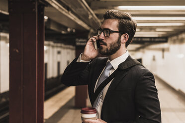 Junger Geschäftsmann, der am Bahnsteig einer U-Bahn-Station wartet und ein Smartphone benutzt - UUF09007