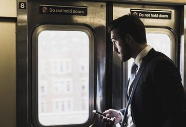 Young businessman taking metro, using smart phone - UUF09009