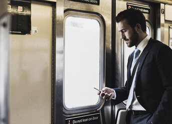 Junger Geschäftsmann fährt mit der U-Bahn und benutzt ein Smartphone - UUF09010