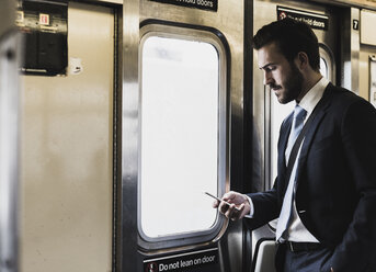 Young businessman taking metro, using smart phone - UUF09010