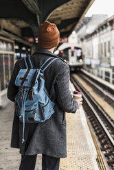 Junger Mann wartet am Bahnsteig einer U-Bahn-Station und hält einen Einwegbecher - UUF09027