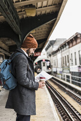 Junger Mann wartet am Bahnsteig einer U-Bahn-Station und liest Dokumente - UUF09028