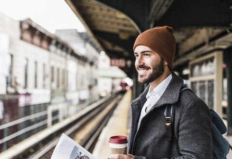 Young man waiting at metro station platform, holding disposable cup - UUF09029