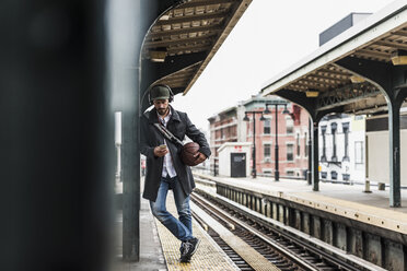 Junger Mann, der am Bahnsteig auf die U-Bahn wartet und sein Smartphone benutzt - UUF09030