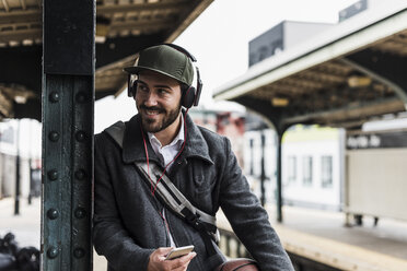Junger Mann, der am Bahnsteig auf die U-Bahn wartet und Kopfhörer trägt - UUF09031