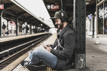 Junger Mann, der am Bahnsteig auf die U-Bahn wartet und sein Smartphone benutzt - UUF09032