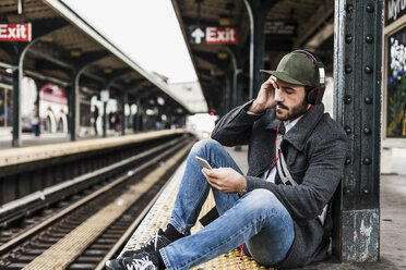 Junger Mann, der am Bahnsteig auf die U-Bahn wartet und sein Smartphone benutzt - UUF09033