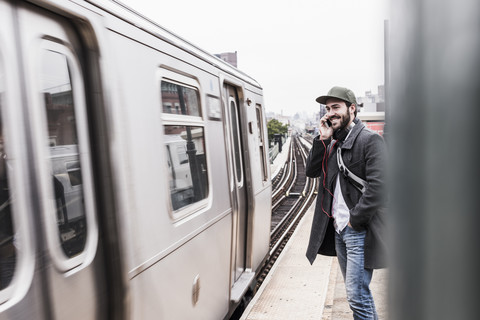 Junger Mann, der am Bahnsteig auf die U-Bahn wartet und sein Smartphone benutzt, lizenzfreies Stockfoto