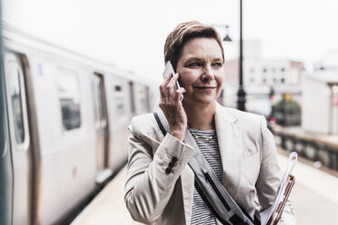 Mature woman using smart phone at commuter train station - UUF09043