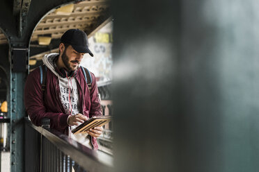 Junger Mann, der auf die U-Bahn wartet, Kopfhörer trägt und ein digitales Tablet benutzt - UUF09046