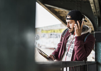 Junger Mann, der auf die U-Bahn wartet, Kopfhörer trägt und ein digitales Tablet benutzt - UUF09047