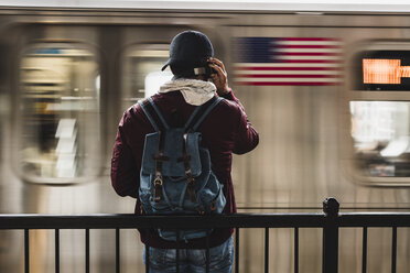Young man waiting for metro at train station platform, wearing headphones - UUF09048