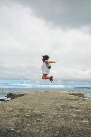 Frau auf Pier springt in die Luft, lizenzfreies Stockfoto