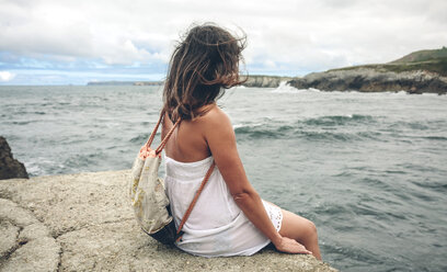 Frau mit Rucksack sitzt auf dem Pier und schaut auf das Meer - DAPF00458
