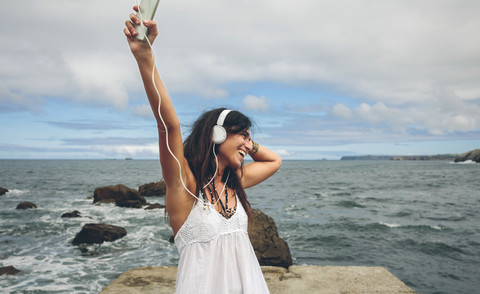 Glückliche Frau auf einer Seebrücke, die mit Kopfhörern Musik hört, lizenzfreies Stockfoto