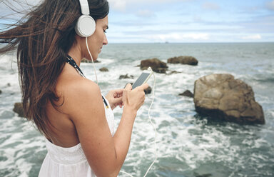 Woman listening music with headphones and smartphone in front of the sea - DAPF00466