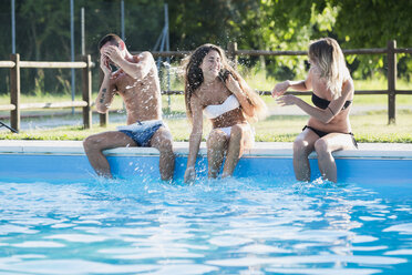 Three friends splashing with water at pool edge - MAUF00898
