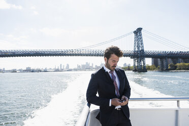USA, New York City, businessman on ferry on East River checking cell phone - UUF09054