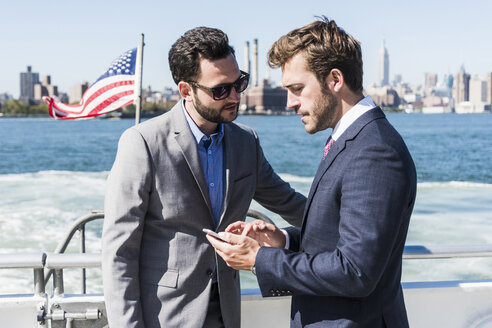 USA, New York City, zwei Geschäftsleute mit Mobiltelefon auf einer Fähre auf dem East River - UUF09060