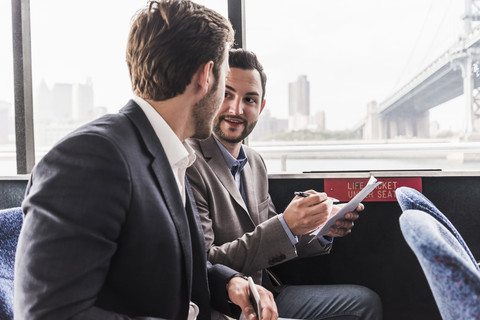 Zwei Geschäftsleute mit Dokument im Gespräch auf dem Passagierdeck einer Fähre, lizenzfreies Stockfoto