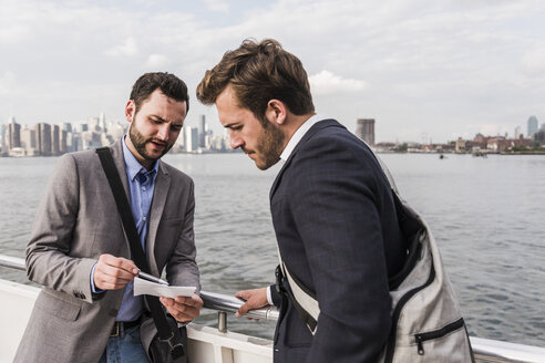 USA, New York City, zwei Geschäftsleute bei der Durchsicht von Dokumenten auf einer Fähre auf dem East River - UUF09097