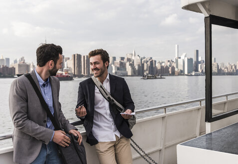 USA, New York City, zwei lächelnde Geschäftsleute unterhalten sich auf einer Fähre auf dem East River - UUF09104