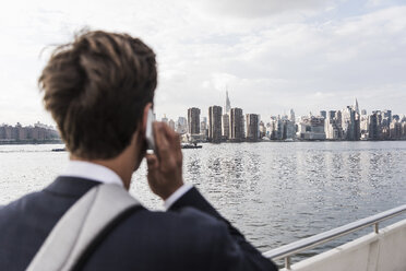 USA, New York City, Rückenansicht eines Mannes am Telefon mit der Skyline von Manhattan im Hintergrund - UUF09106