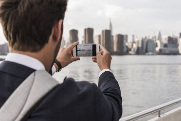 USA, New York City, Rückansicht eines Mannes am East River beim Fotografieren mit dem Handy - UUF09107