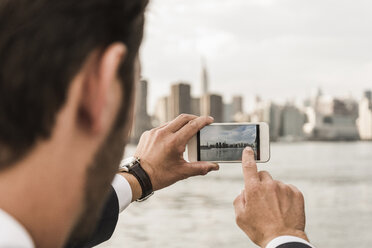 USA, New York City, Mann am East River, der mit seinem Handy ein Foto von Manhattan macht - UUF09108