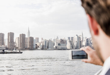 USA, New York City, Mann am East River, der mit seinem Handy ein Foto von Manhattan macht - UUF09109