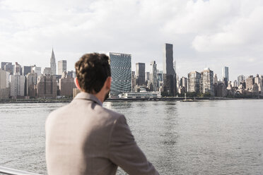 USA, New York City, Rückenansicht eines Mannes am East River mit Blick auf Manhattan - UUF09116