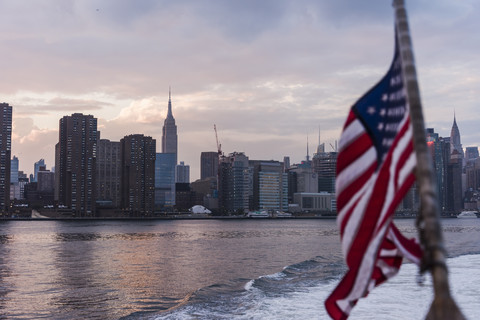 USA, New York City, US-Flagge auf einer Fähre auf dem East River mit der Skyline von Manhattan im Hintergrund, lizenzfreies Stockfoto