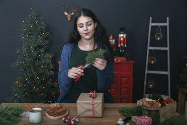 Junge Frau schneidet einen Zweig für die Dekoration eines Weihnachtsgeschenks - RTBF00496