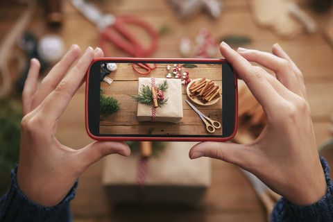 Woman photographing decorated Christmas gift with smartphone, close-up stock photo